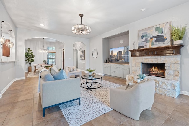 4801 Pyrenees Pass, Bee Cave, TX 78738 - living room featuring arched walkways, a chandelier, baseboards, a stone fireplace, and light tile patterned floors