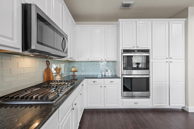 kitchen featuring visible vents, decorative backsplash, appliances with stainless steel finishes, dark wood-type flooring, and white cabinetry