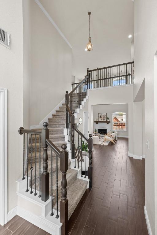 staircase featuring a towering ceiling, visible vents, baseboards, and wood finished floors