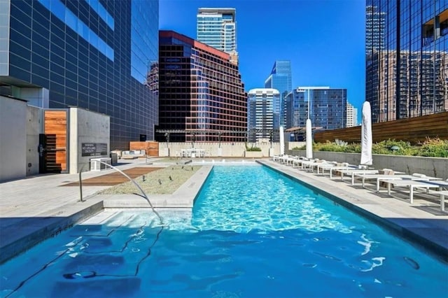 community pool with a view of city, a patio area, and fence