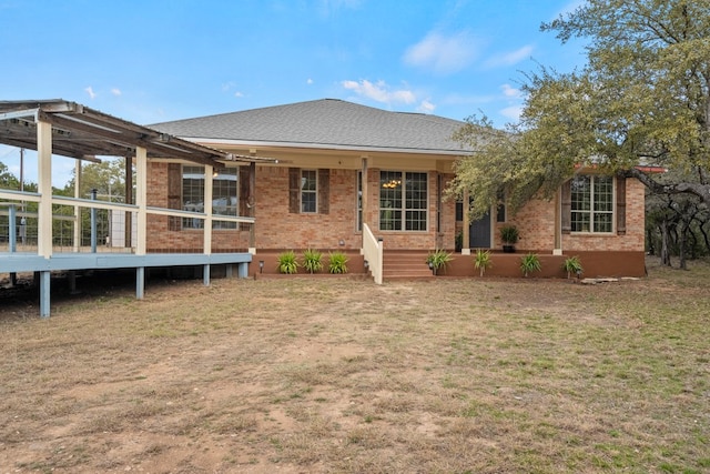 rear view of property with a yard, roof with shingles, and brick siding