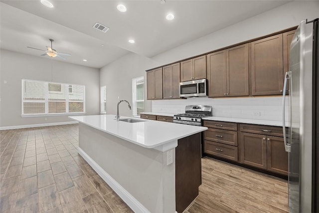 kitchen featuring appliances with stainless steel finishes, a sink, a kitchen island with sink, and decorative backsplash