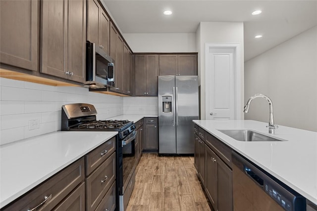 kitchen with dark brown cabinets, stainless steel appliances, a sink, and light countertops