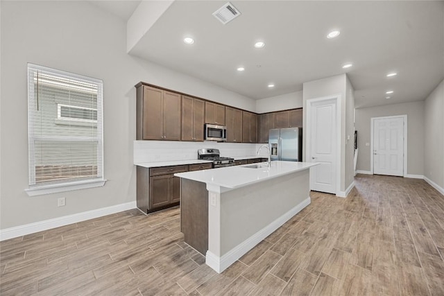 kitchen featuring appliances with stainless steel finishes, visible vents, an island with sink, and light wood finished floors