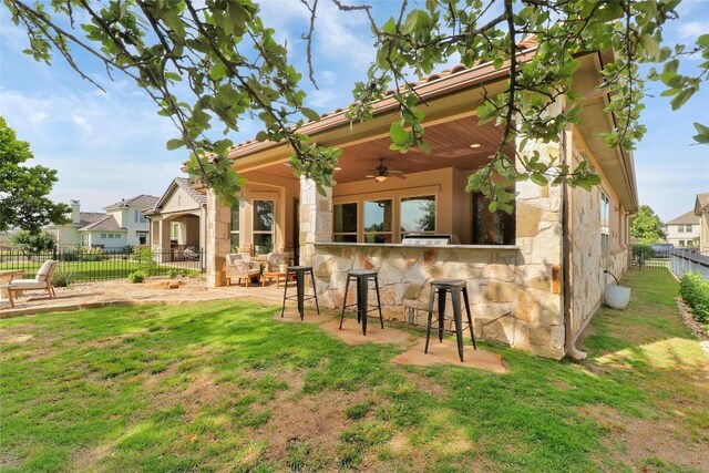 rear view of property featuring stone siding, a ceiling fan, a patio, and a bar