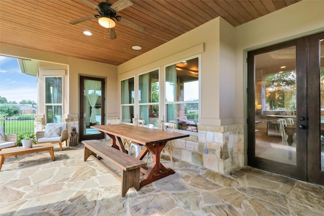 sunroom with stone floors, wood ceiling, and a wainscoted wall