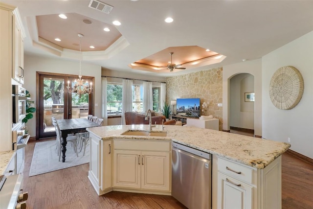 kitchen featuring stainless steel appliances, a sink, arched walkways, a raised ceiling, and light wood-type flooring