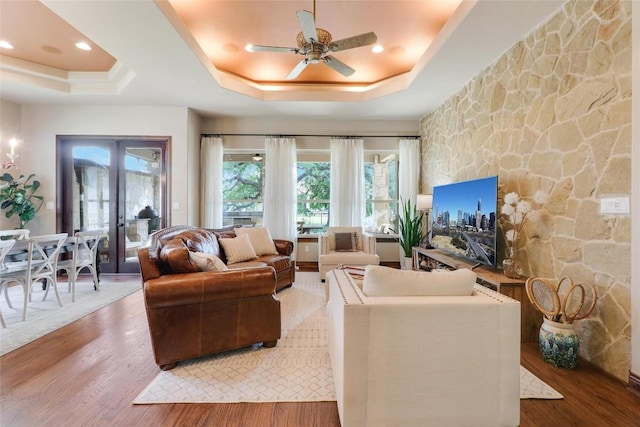 living area featuring a raised ceiling, wood finished floors, french doors, and a ceiling fan