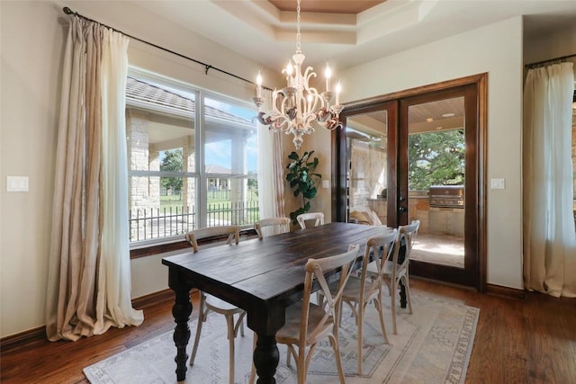 dining room featuring a chandelier, wood finished floors, baseboards, french doors, and a raised ceiling
