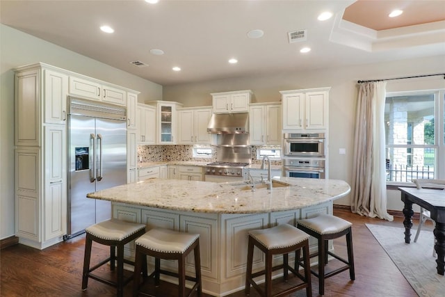 kitchen featuring stainless steel appliances, under cabinet range hood, a breakfast bar area, dark wood-type flooring, and a sink
