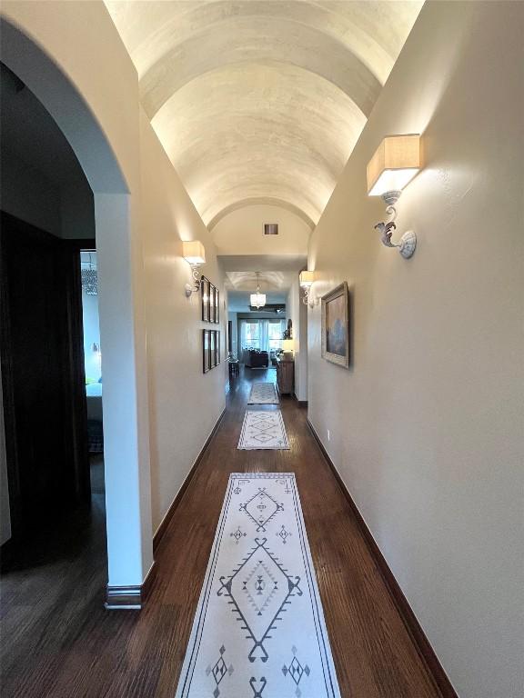 hallway with lofted ceiling, dark wood-style flooring, arched walkways, and baseboards