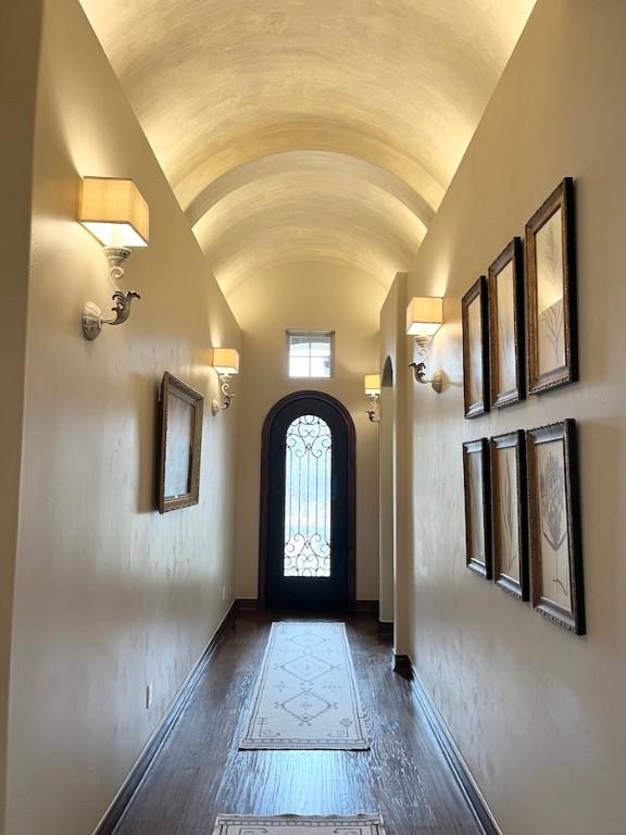 entryway with arched walkways, dark wood-type flooring, baseboards, and high vaulted ceiling