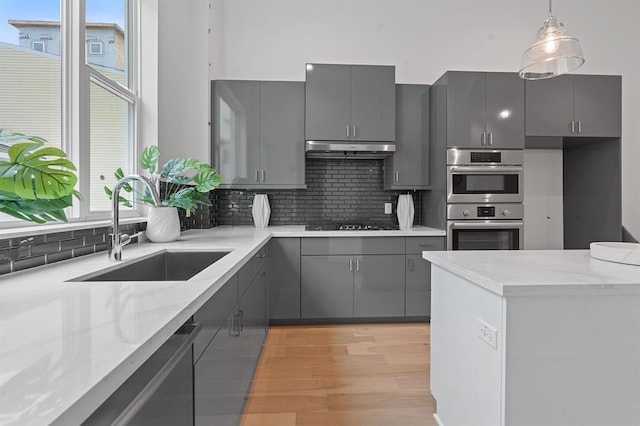 kitchen featuring a sink, gray cabinets, under cabinet range hood, double oven, and backsplash