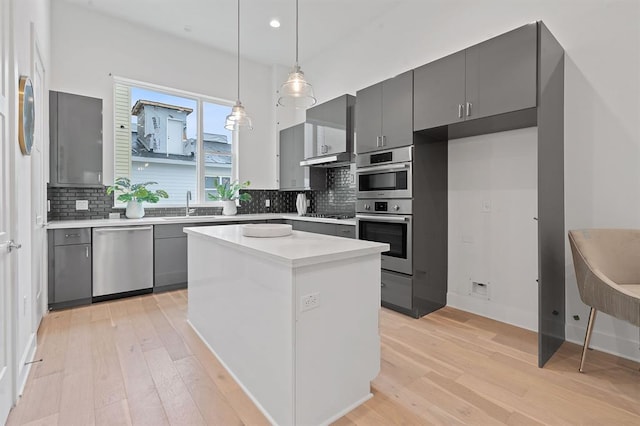 kitchen featuring stainless steel appliances, a sink, hanging light fixtures, backsplash, and light wood finished floors