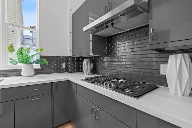 kitchen featuring tasteful backsplash, stainless steel gas cooktop, ventilation hood, and gray cabinetry