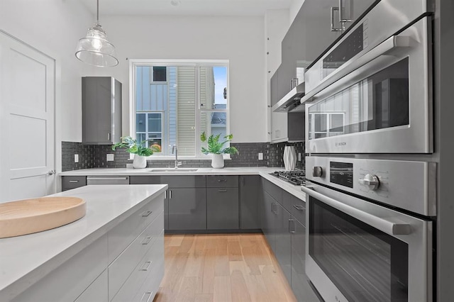 kitchen with gray cabinets, light countertops, a sink, and backsplash