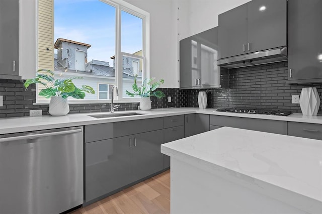 kitchen with under cabinet range hood, gray cabinetry, a sink, gas stovetop, and stainless steel dishwasher