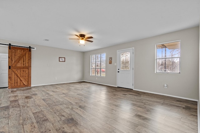 unfurnished living room with wood finished floors, ceiling fan, baseboards, and a barn door