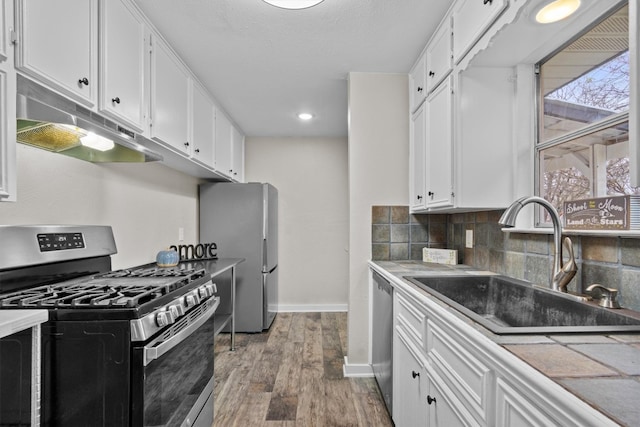 kitchen featuring appliances with stainless steel finishes, white cabinetry, a sink, and under cabinet range hood