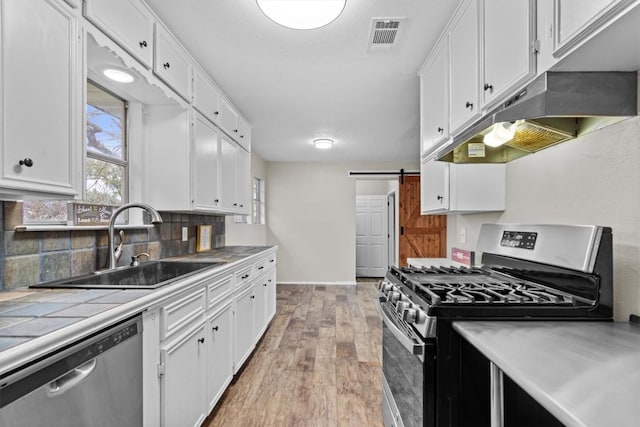 kitchen featuring a barn door, stainless steel appliances, a sink, white cabinetry, and tile counters