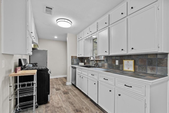 kitchen with appliances with stainless steel finishes, backsplash, a sink, and white cabinets