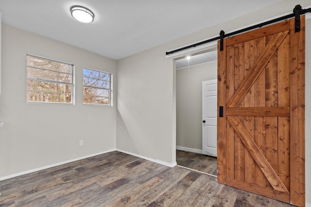 unfurnished bedroom featuring a barn door, wood finished floors, and baseboards