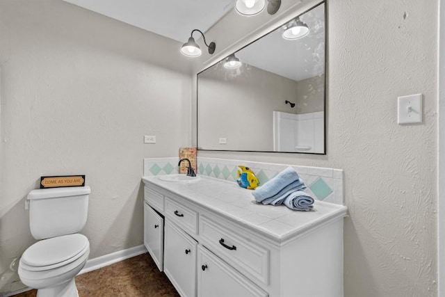 bathroom featuring tasteful backsplash, baseboards, a textured wall, toilet, and vanity