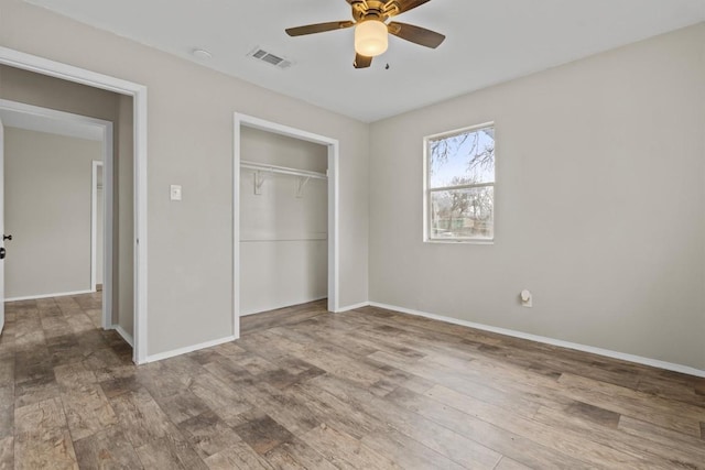 unfurnished bedroom with a closet, wood finished floors, visible vents, and baseboards