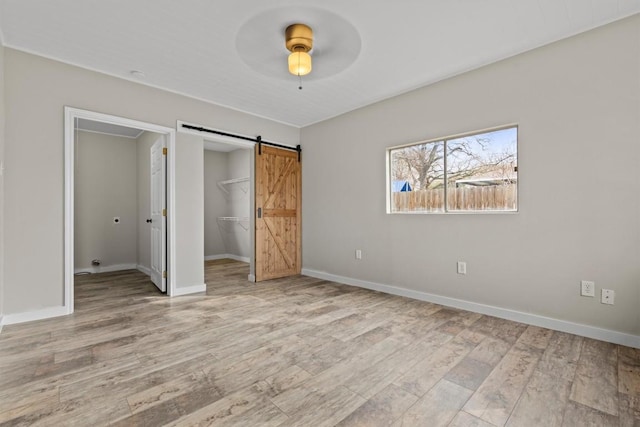 unfurnished bedroom with a barn door, baseboards, light wood-style flooring, a spacious closet, and a closet