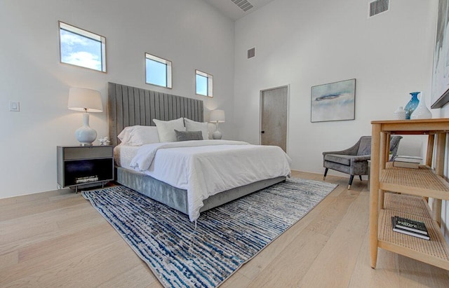 bedroom with a high ceiling, visible vents, and wood finished floors