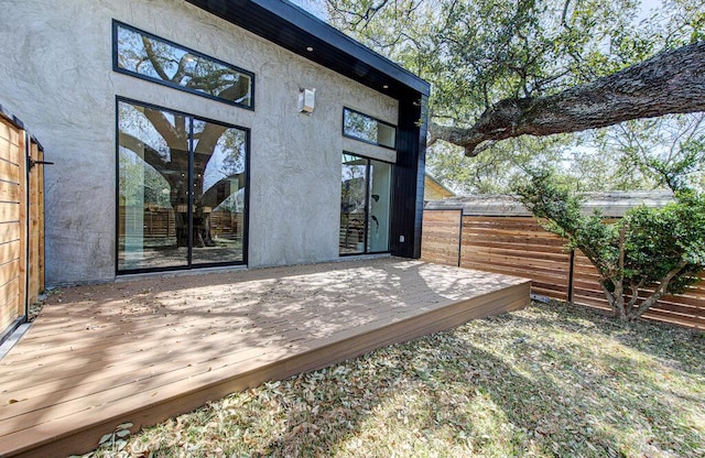 entrance to property featuring a deck, fence, and stucco siding