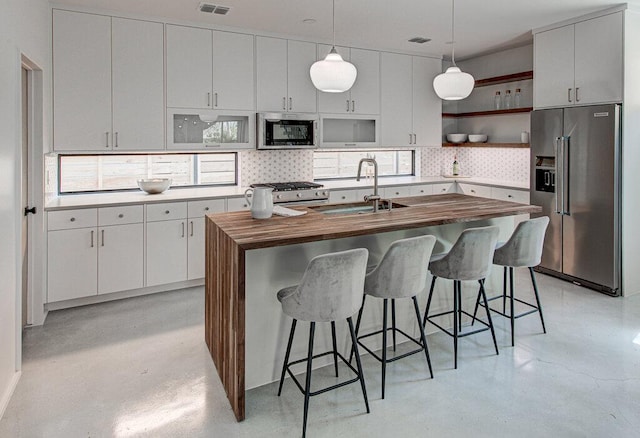 kitchen featuring open shelves, backsplash, appliances with stainless steel finishes, a sink, and wood counters