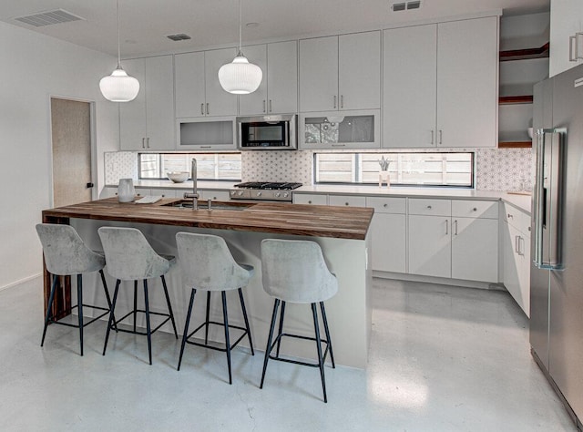 kitchen with visible vents, decorative backsplash, stainless steel appliances, wooden counters, and a sink