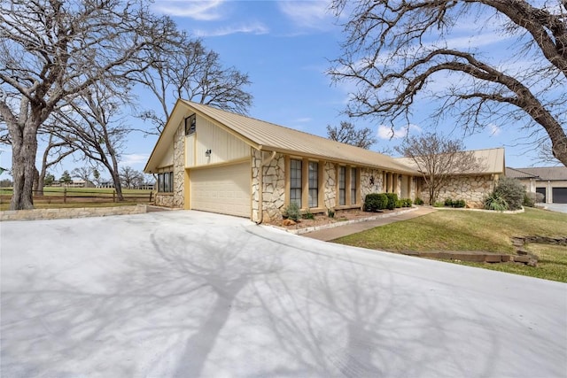 view of front of property featuring a garage, stone siding, driveway, and a front lawn