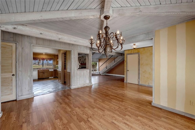 unfurnished dining area with baseboards, stairway, wood finished floors, beamed ceiling, and a chandelier