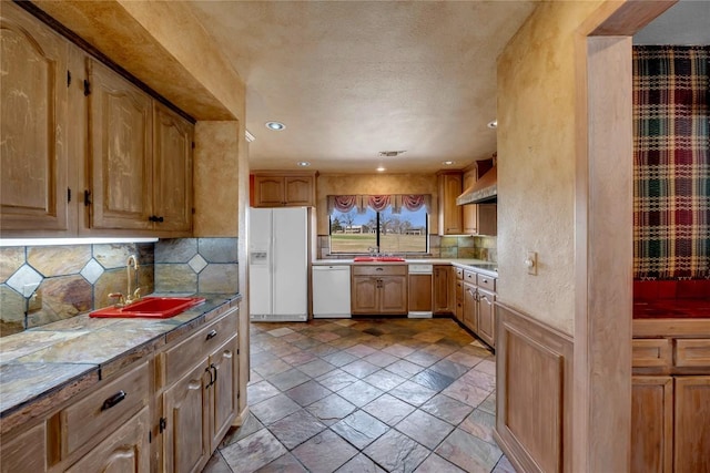 kitchen featuring white appliances, wall chimney exhaust hood, a sink, light countertops, and backsplash