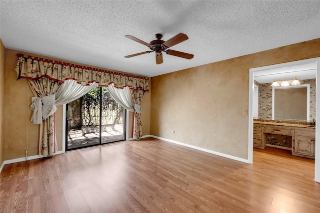 spare room featuring light wood-type flooring, a textured ceiling, baseboards, and a ceiling fan