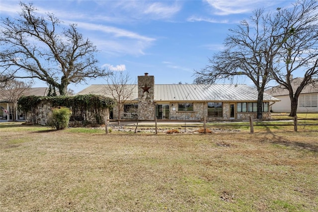 view of front of home featuring a standing seam roof, metal roof, stone siding, a front lawn, and a chimney