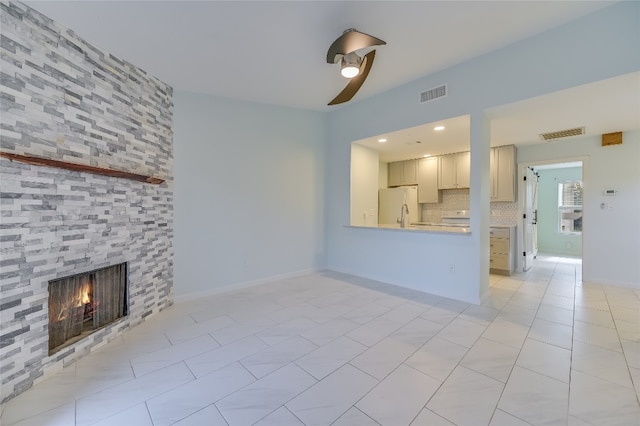 unfurnished living room featuring light tile patterned floors, visible vents, a ceiling fan, a large fireplace, and baseboards