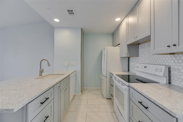 kitchen with a peninsula, white appliances, a sink, visible vents, and decorative backsplash