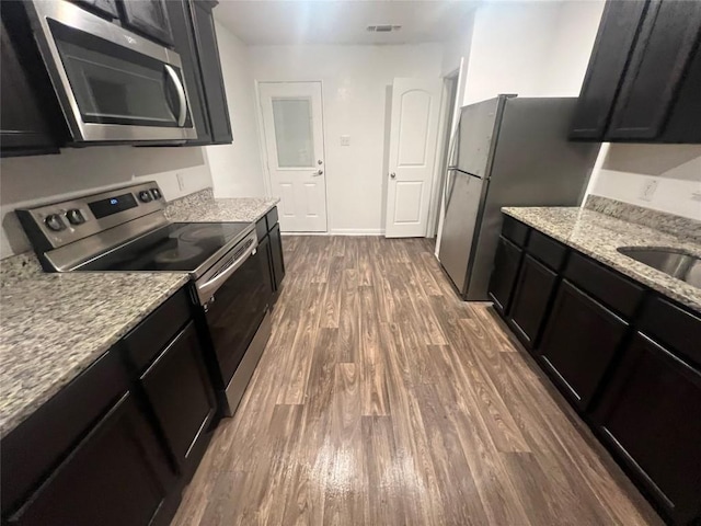 14009 John Aregood Pass, Elgin, TX 78621 - kitchen featuring stainless steel appliances, dark wood-style flooring, dark cabinetry, and light stone countertops
