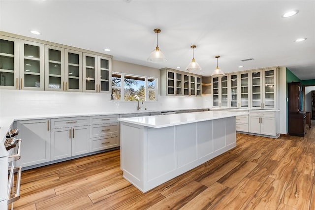 kitchen with a center island, tasteful backsplash, light countertops, light wood-style flooring, and glass insert cabinets