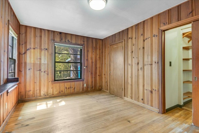 spare room featuring wooden walls, baseboards, and light wood finished floors