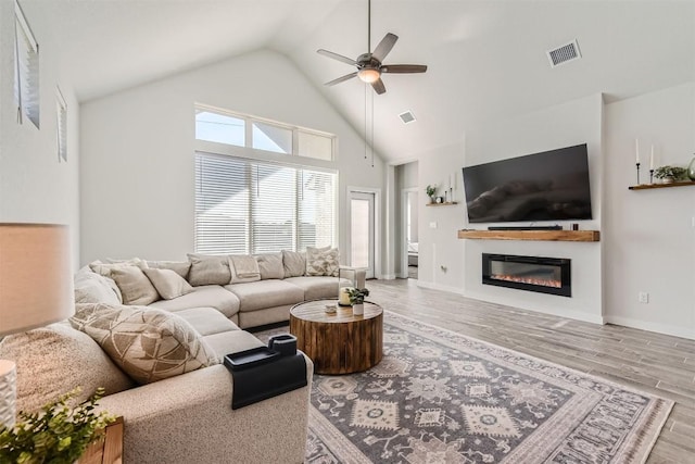 living area with high vaulted ceiling, a glass covered fireplace, wood finished floors, and visible vents