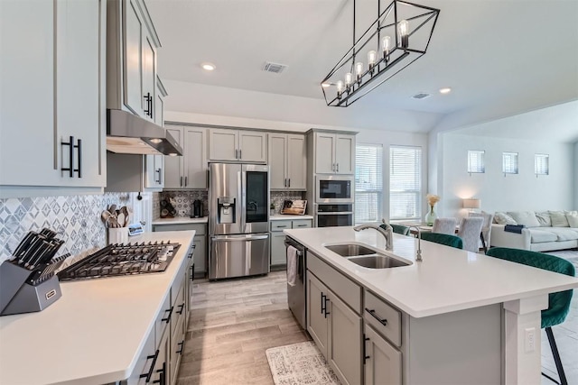 kitchen featuring gray cabinetry, under cabinet range hood, stainless steel appliances, a sink, and open floor plan