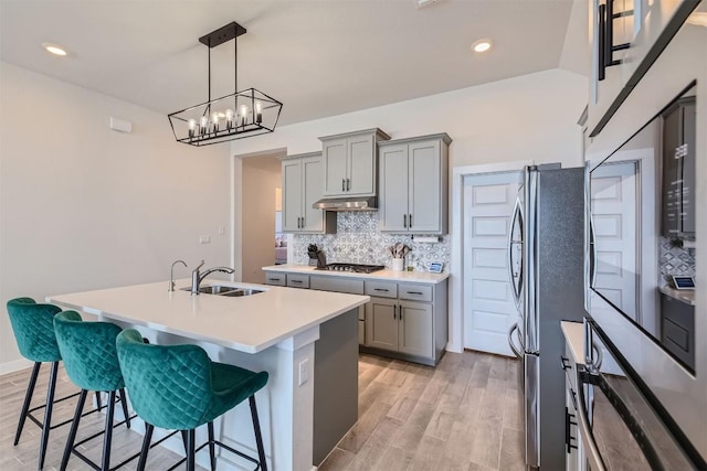 kitchen featuring tasteful backsplash, appliances with stainless steel finishes, gray cabinets, under cabinet range hood, and a sink