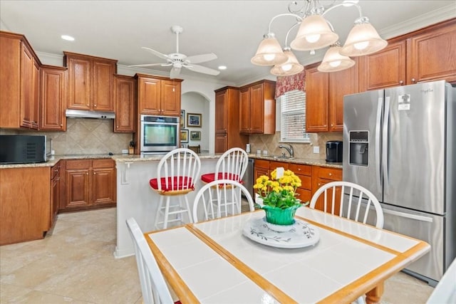 kitchen with appliances with stainless steel finishes, brown cabinetry, ornamental molding, and under cabinet range hood