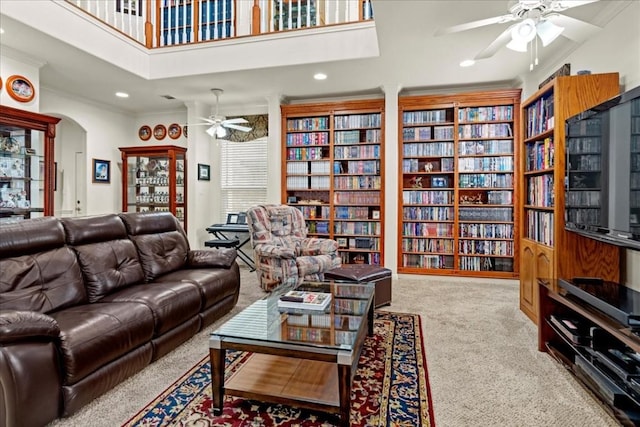 living room featuring arched walkways, carpet flooring, a ceiling fan, wall of books, and crown molding