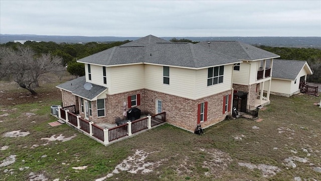 exterior space featuring brick siding, cooling unit, and roof with shingles