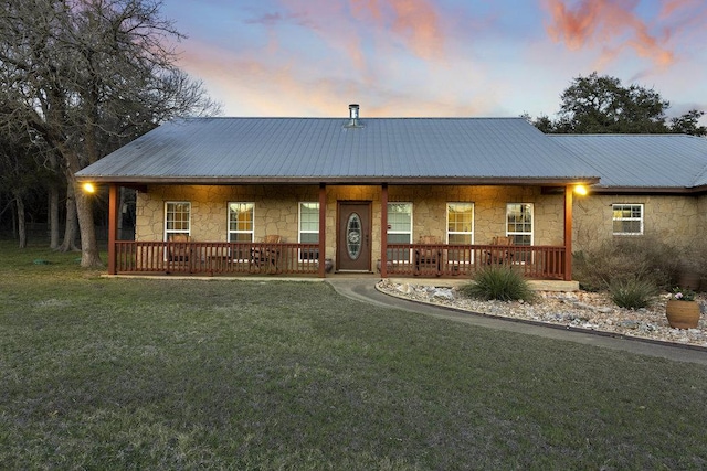 view of front facade with metal roof, stone siding, a yard, and covered porch